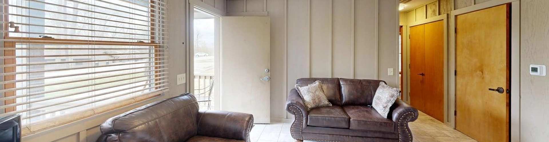 ADA living room. The room is spacious with two small couches perpendicular from each other against the walls. In the space between the couches in the corner of the room is the front door. Behind one of the couches is a hallway with doors lining the wall.