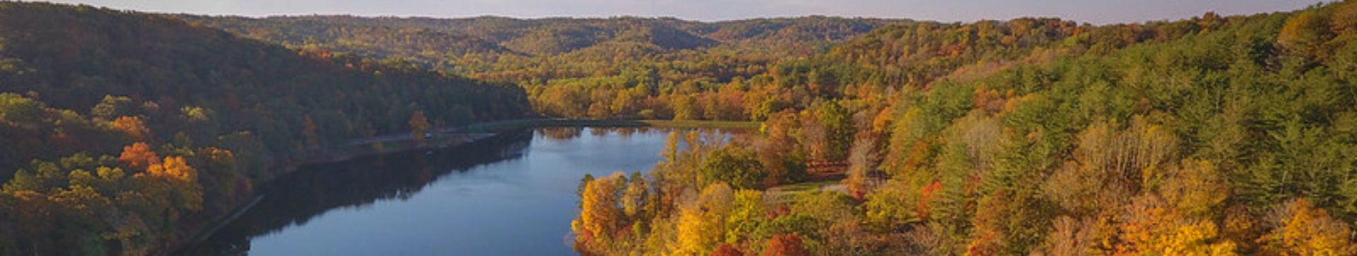 Scenic aerial view of Lake Hope surrounded by rolling forested hills dressed in vibrant fall colors. The calm lake reflects the autumn landscape, showcasing the natural beauty of southeastern Ohio.